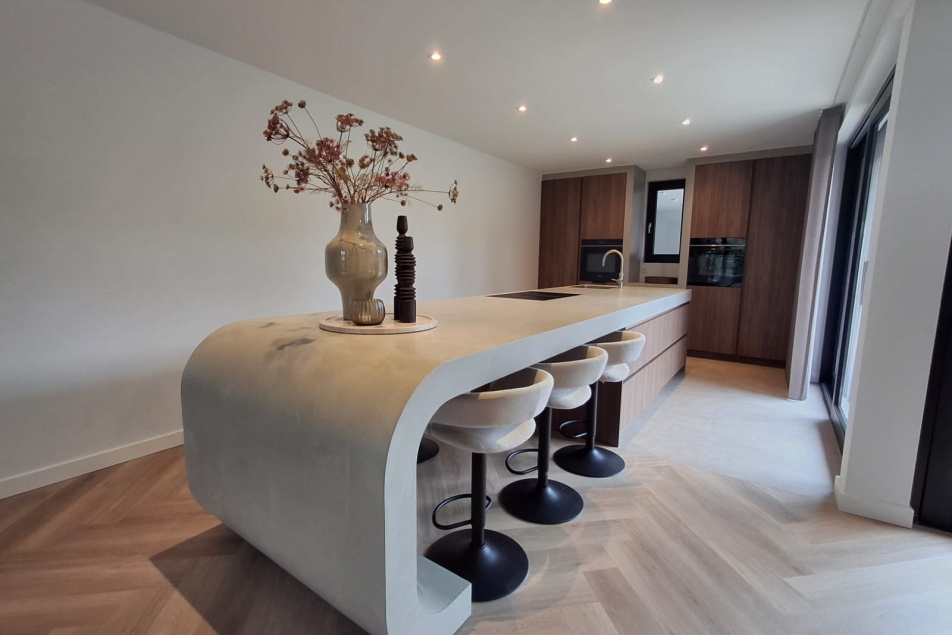 Moderne keuken met afgerond kookeiland in beton ciré en houtfineer – Thomas Bos Interieurbouw.